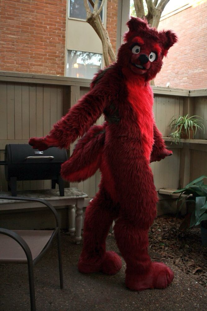 A red wolf fursuiter posing on a fenced-in patio.