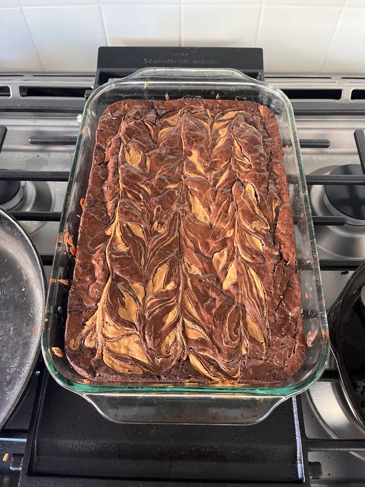 A glass pan holds a tray of brownies that are swirled with peanut butter before baking 