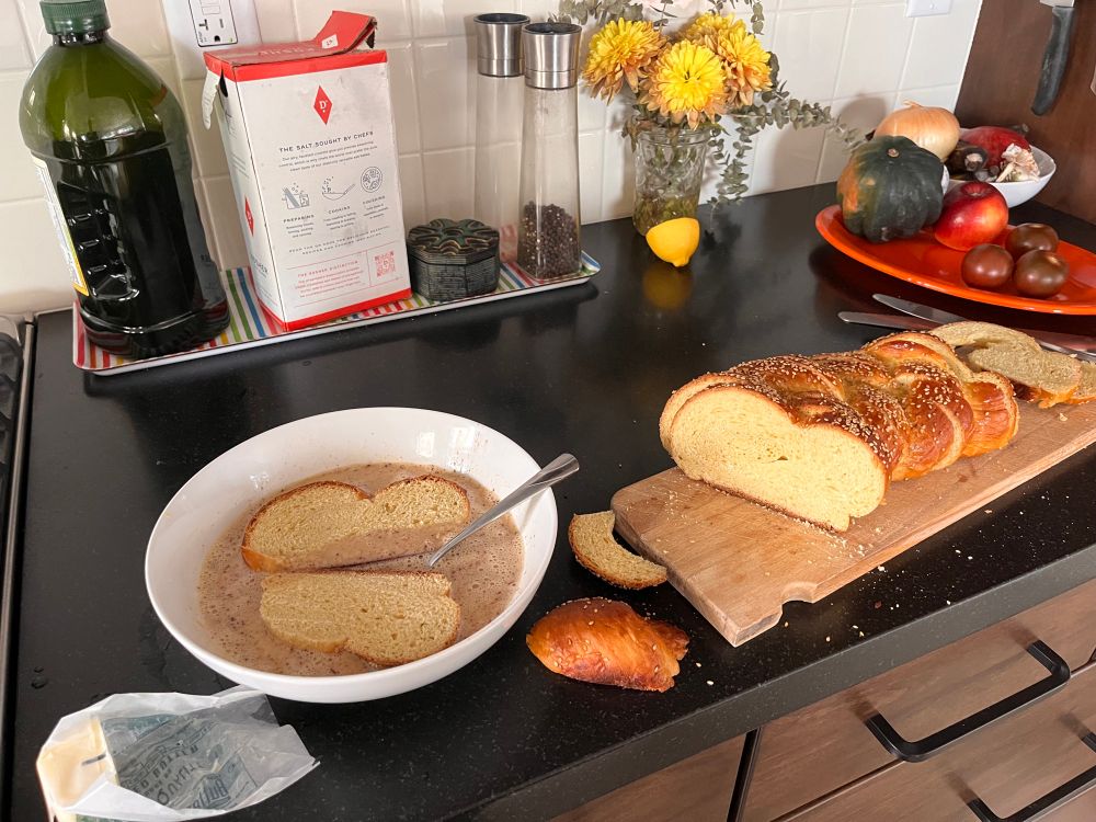 Sliced challah going into an egg batter. Random kitchen stuff on the counter like salt and oil and a half a lemon and an acorn squash 