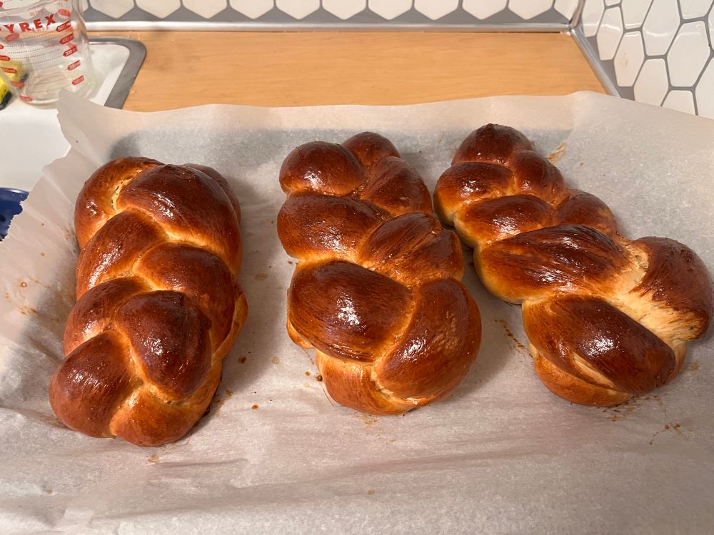 Three loaves of shiny golden challah on a sheet of parchment paper 