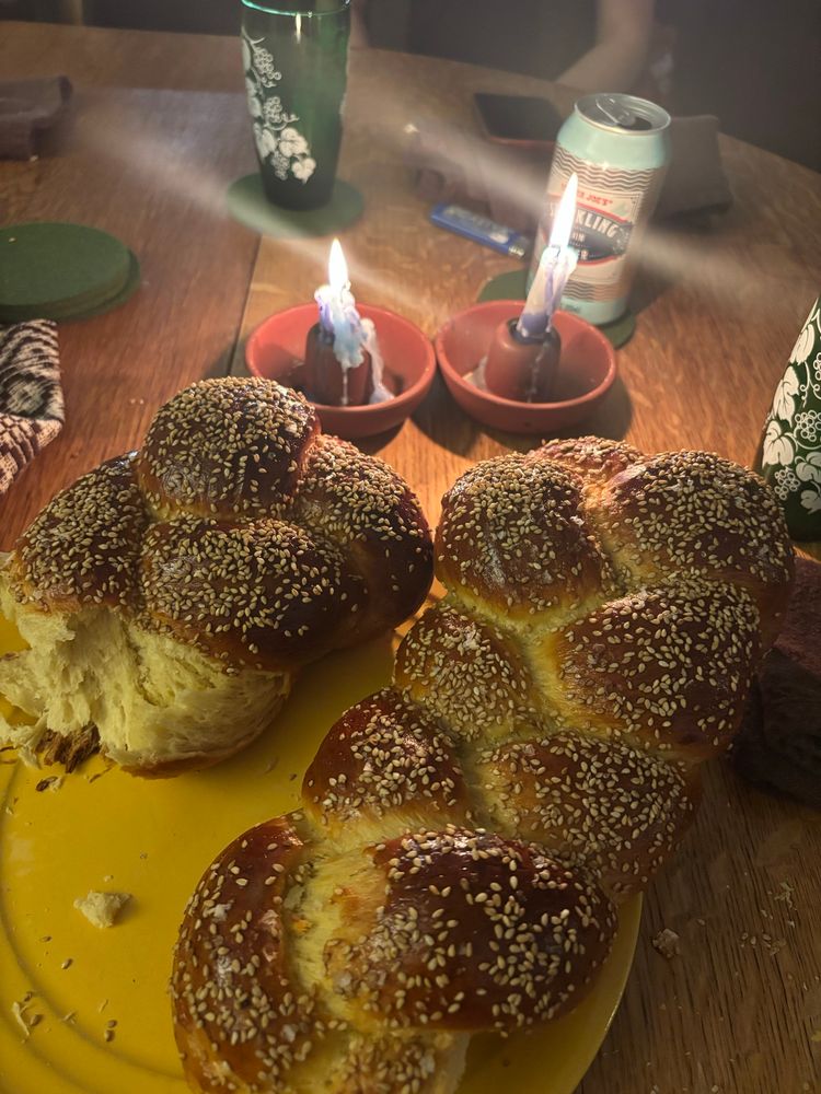 1.5 challahs on a yellow plate, Shabbat candles and various drinks on a wooden table 