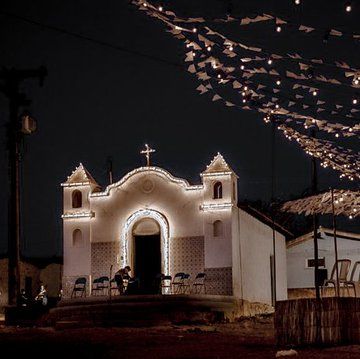 pequena igreja do interior iluminada por luzes e bandeirinhas em uma noite de festa