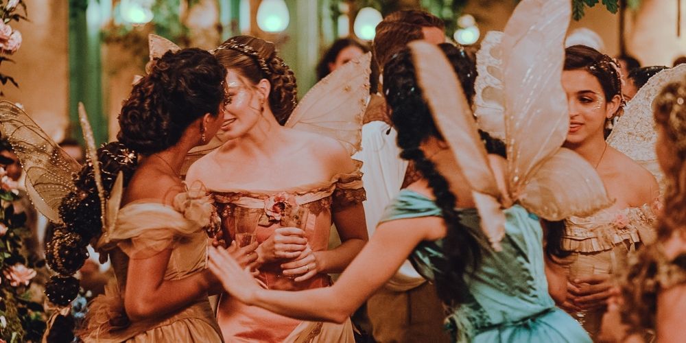 Meninas em roupas de epoca com vestidos longos e asas interagindo numa festa em tons pastéis de azul, rosa e laranja 