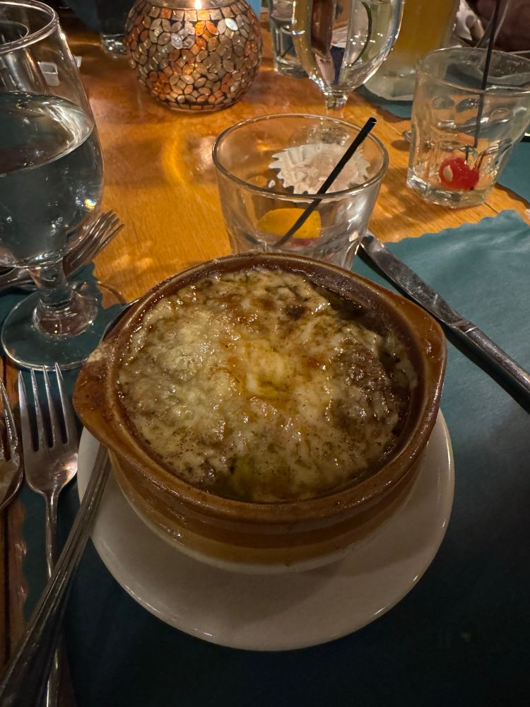 A heaping bowl of French onion soup next to an empty old fashioned sour