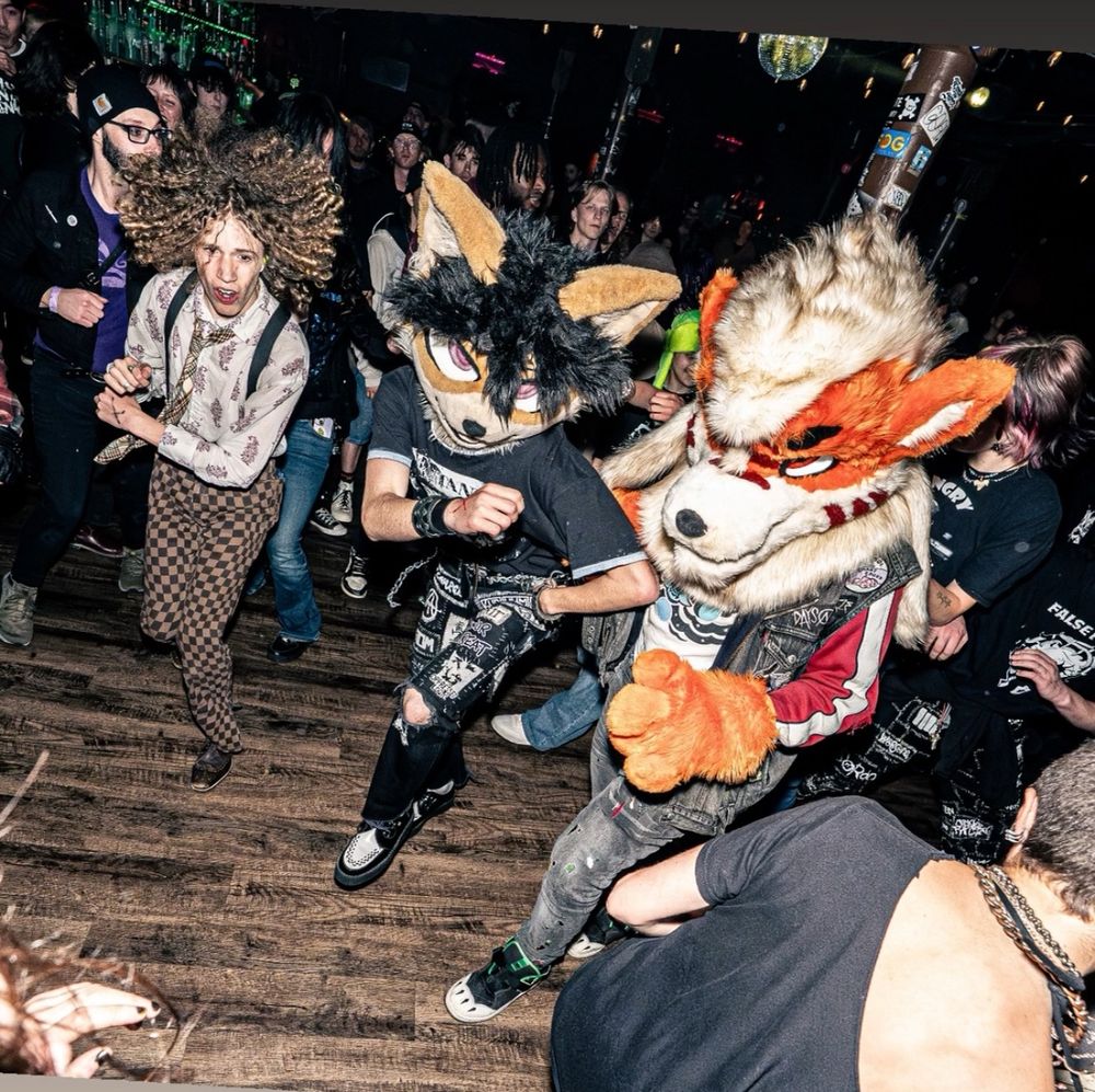 Me and Hana (a Shiba Inu with black hair) fursuiting in the pit together. Hana has pants with a ton of patches, and I’m wearing pants embroidered with thread to look like multicolored paint stains and set of paw shoes that weren’t visible from the previous shot.