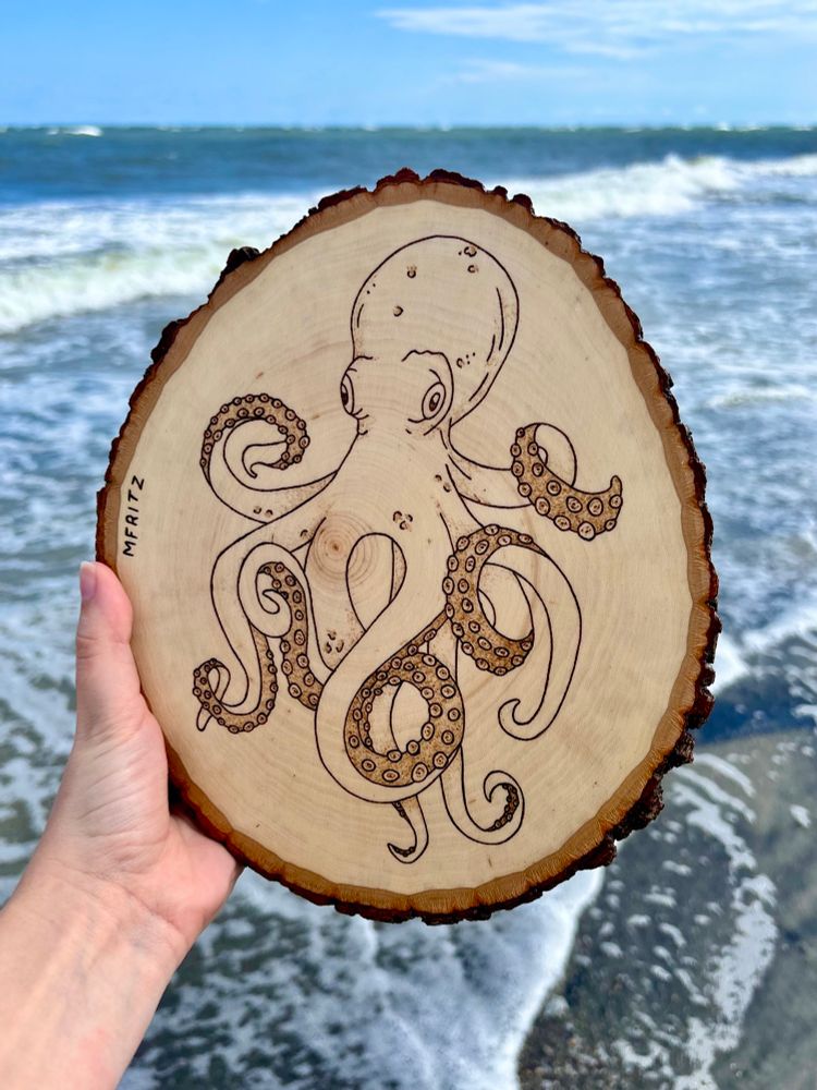 Pyrography of an octopus on a wood slice held in front of the Atlantic Ocean