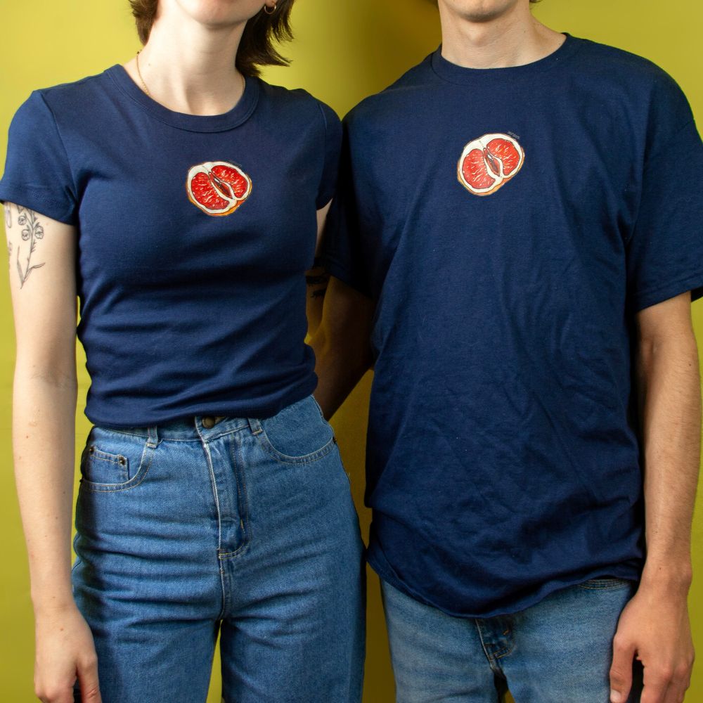Two people standing in front of a yellow background modeling a navy baby tee and regular tshirt with a grapefruit yoni design that was drawn with alcohol markers