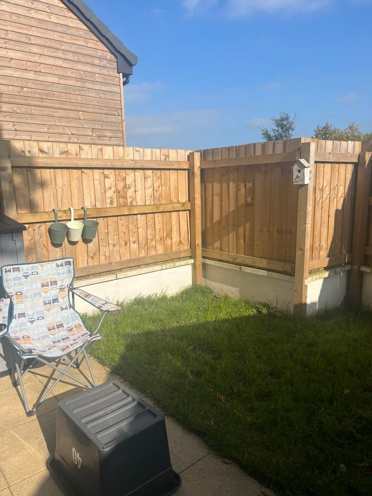 A small garden patch of grass and little patio with a camping chair , bird house on fence 