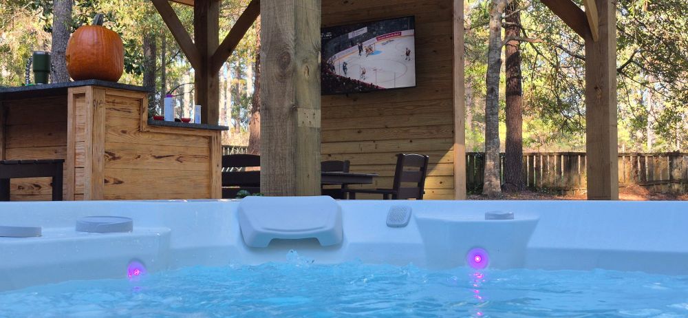 A view of an outdoor TV from a hot tub with a jack o lantern sitting on a bar halfway between 