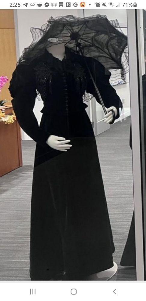 À headless mannequin wears a full length plain black dress and holds a black parasol opened over the left shoulder. It was part of an exhibit of mourning attire put together by a student of fashion history, with the title "Death Becomes Her." 

Photo Contributed by Madison Koellermeier 

https://damchic.orangemedianetwork.com/2966/articles/campus-fashion/historical-mourning-dress-collection-titled-death-becomes-her-on-display-in-austin-hall/