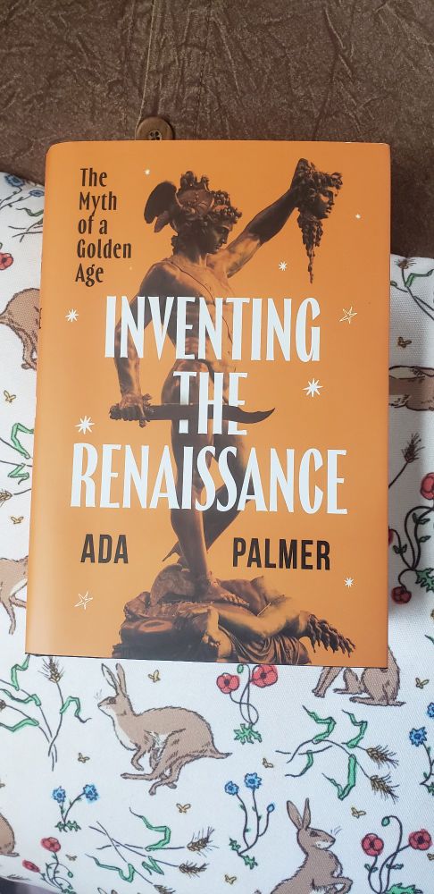 Front cover of the book Inventing the Renaissance: The Myth of a Golden Age, by Ada Palmer, resting on a pillow printed in Hares and Flowers, a pattern of illustrations by Kathleen Jennings. 