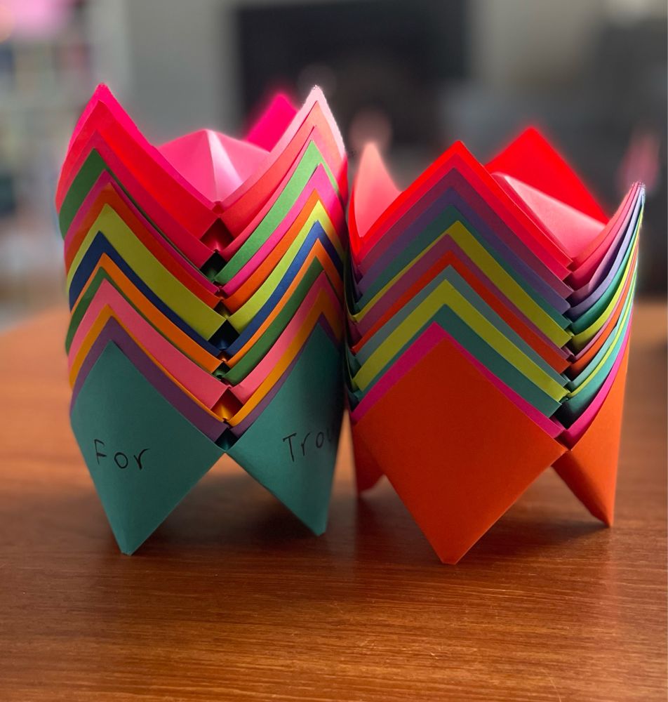 Two stacks of folded paper fortune tellers, in a rainbow of colours