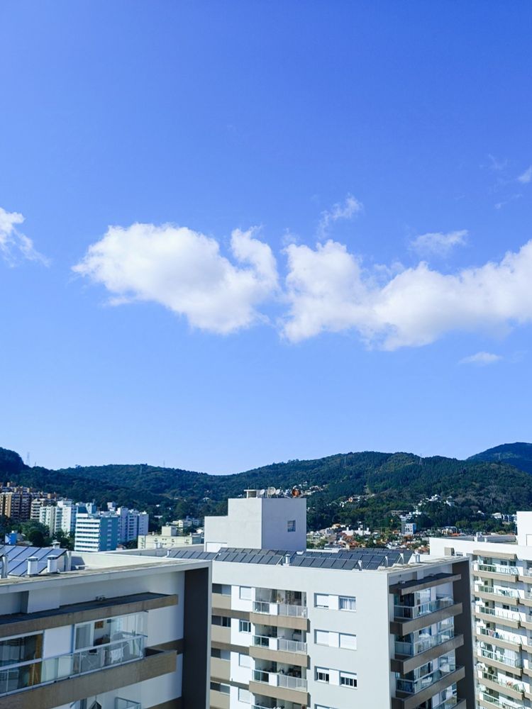 Morro da Lagoa da Conceição com céu azul, nuvens e prédios
