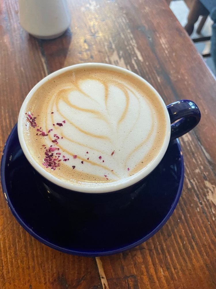 A latte in a blue mug with red flakes and a leaf pattern (I think?) from steamed milk.  
