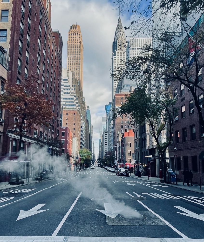Urban street with tall buildings and rising steam from a manhole.
