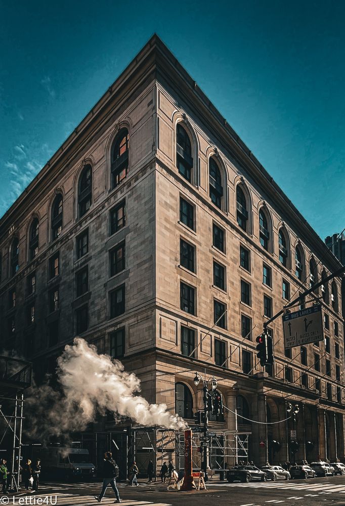 a multi-story building with arched windows, a cloud of steam from an orange vent, and pedestrians at a crosswalk.