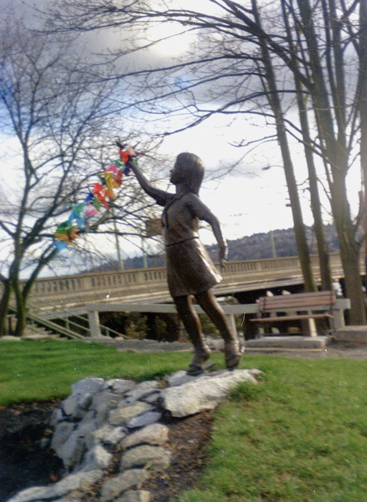 A bronze statue, Sadako and the Thousand Paper Cranes, standing in Seattle's Peace Park. The statue depicts a little girl, Sadako Sasaki, holding up an origami crane. Since this picture was taken, the statue has been stolen and not replaced.