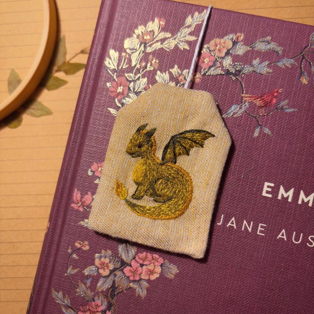 Bookmark in the shape of a tea bag, with a green dragon embroidered on it.