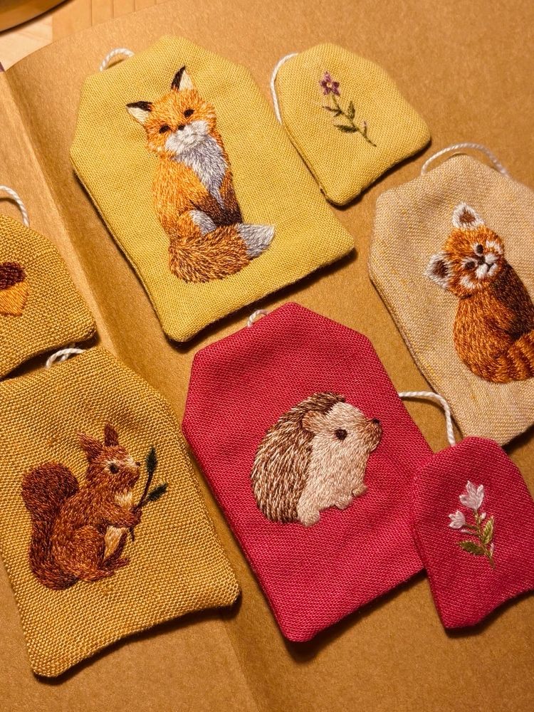 Embroidered bookmarks in the shape of tea bags. The animals embroidered are a squirrel, fox, hedgehog and red panda.