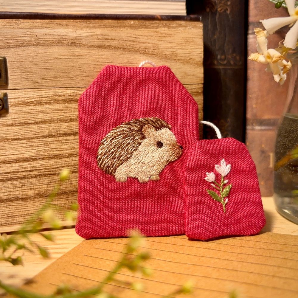 Bookmark in the shape of a tea bag, with a hedgehog embroidered on it.