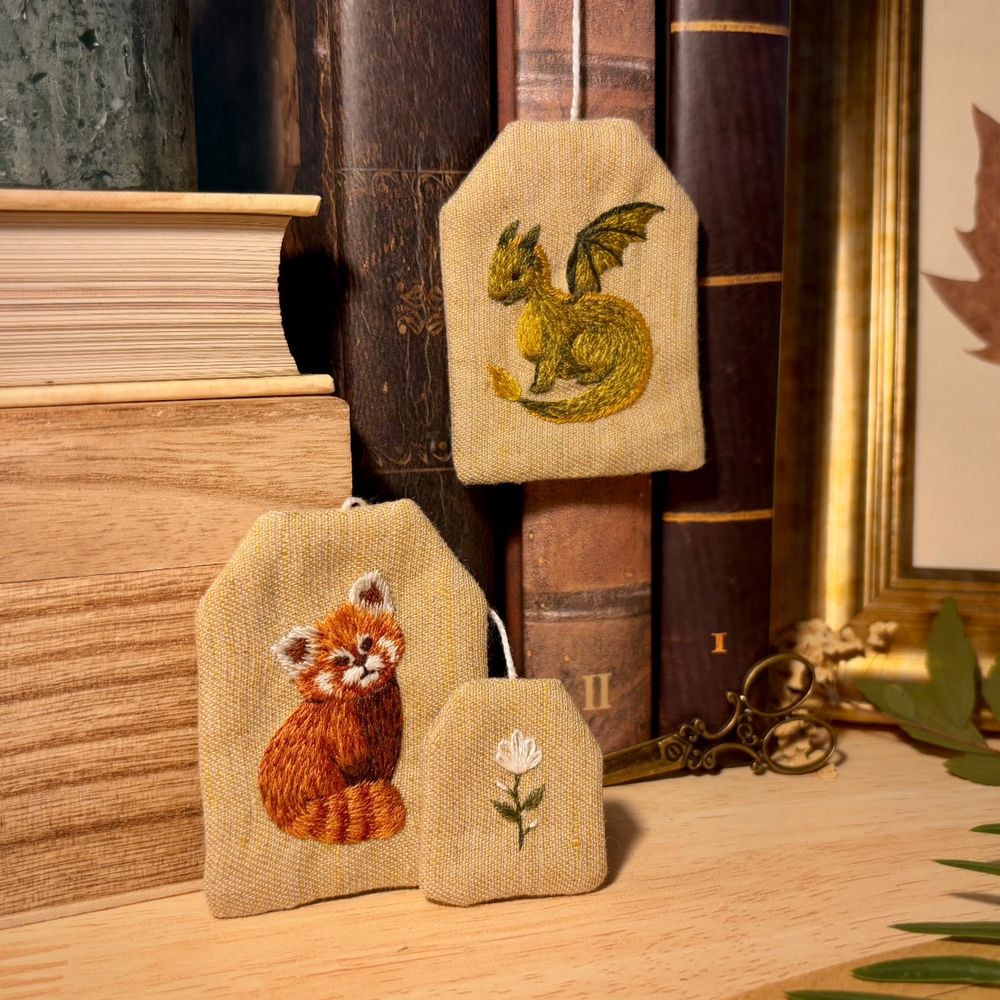 Bookmarks shaped as tea bags. They have embroidery on them: red panda and green dragon.
