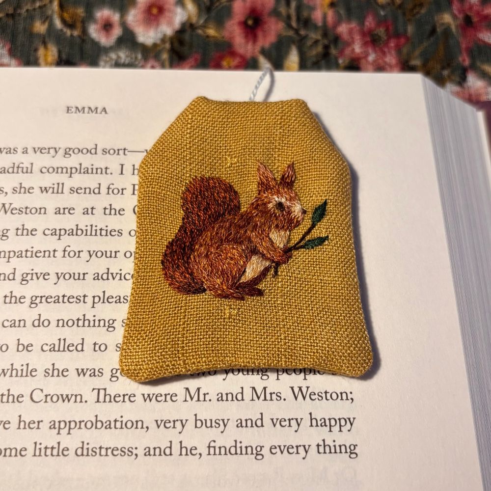 Bookmark made out of green fabric, shaped as a tea bag. There's a squirrel embroidered on it.