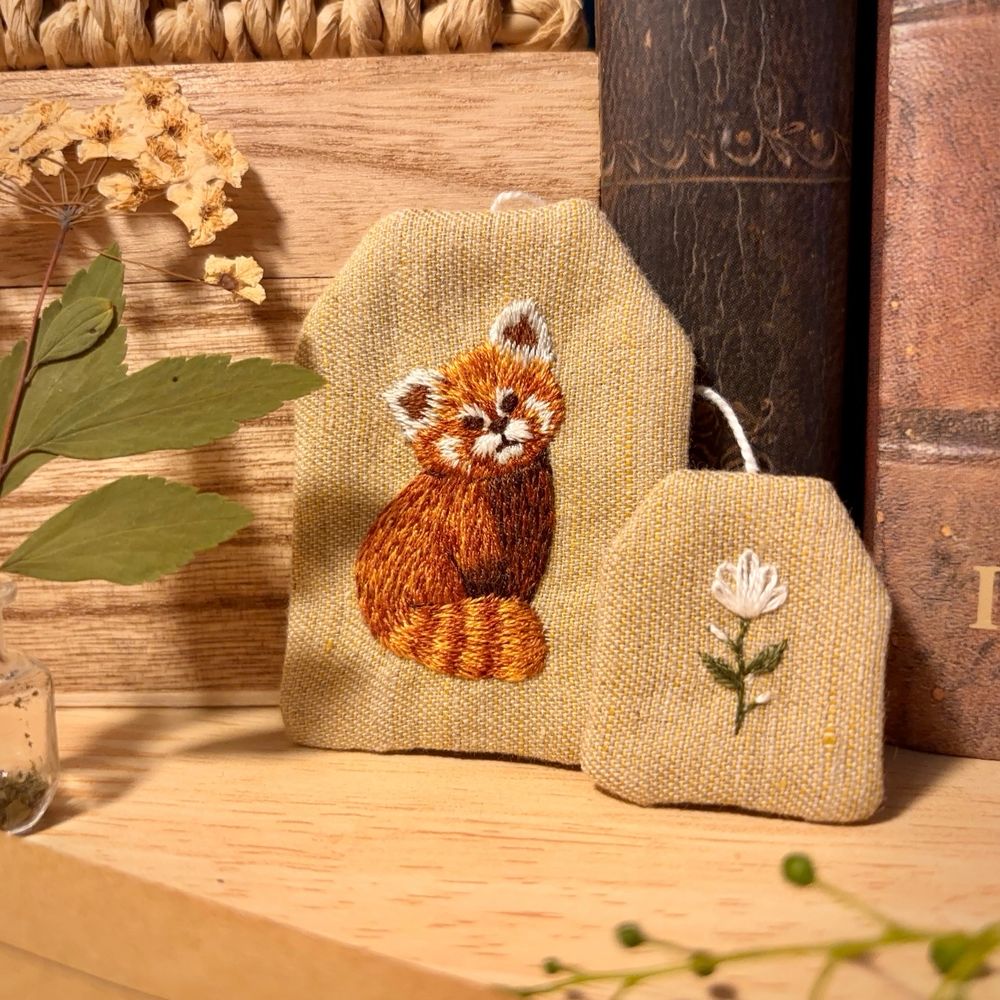 Bookmark in the shape of a tea bag, with a red panda embroidered on it.