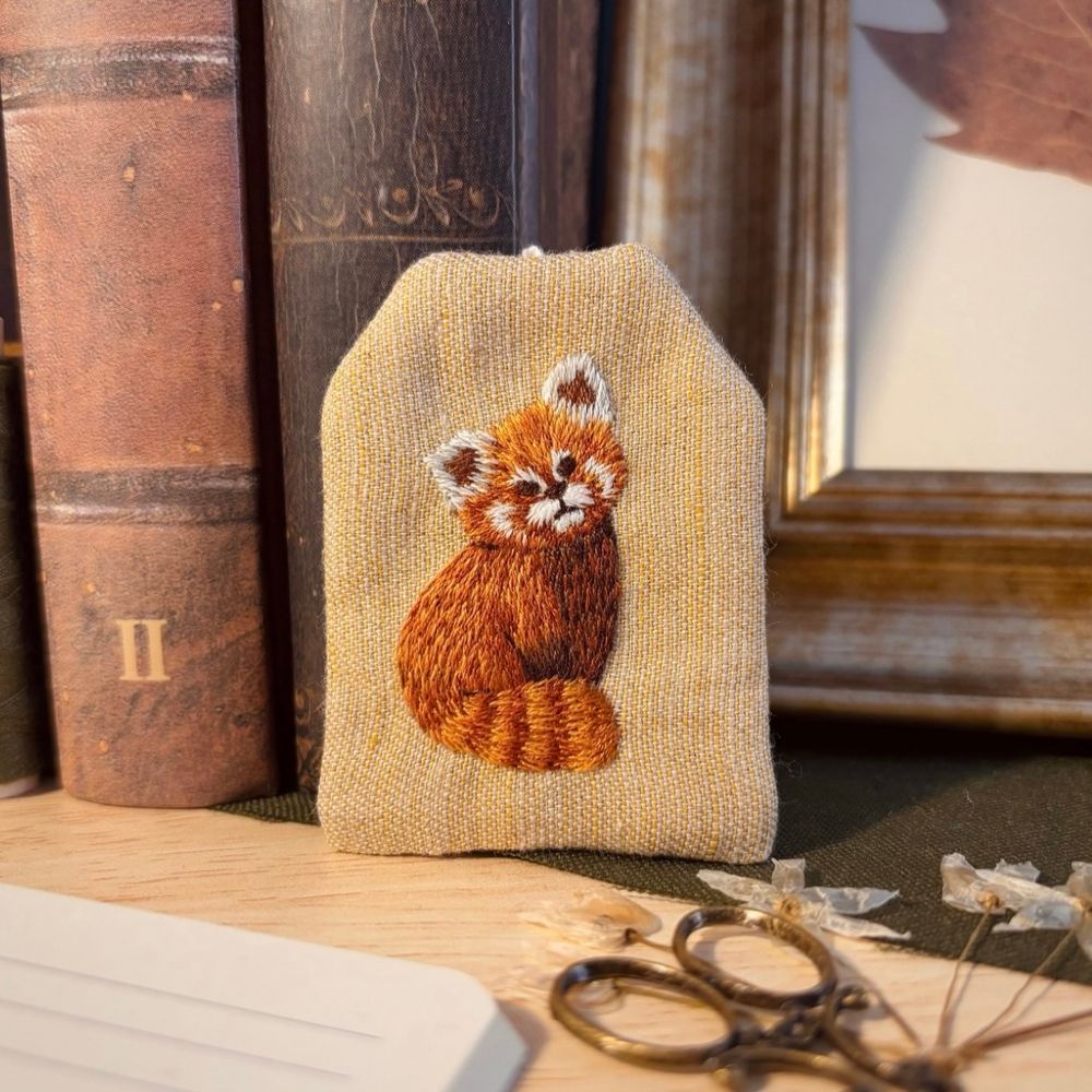 Bookmark shaped as a tea bag, with a red panda embroidered on it.