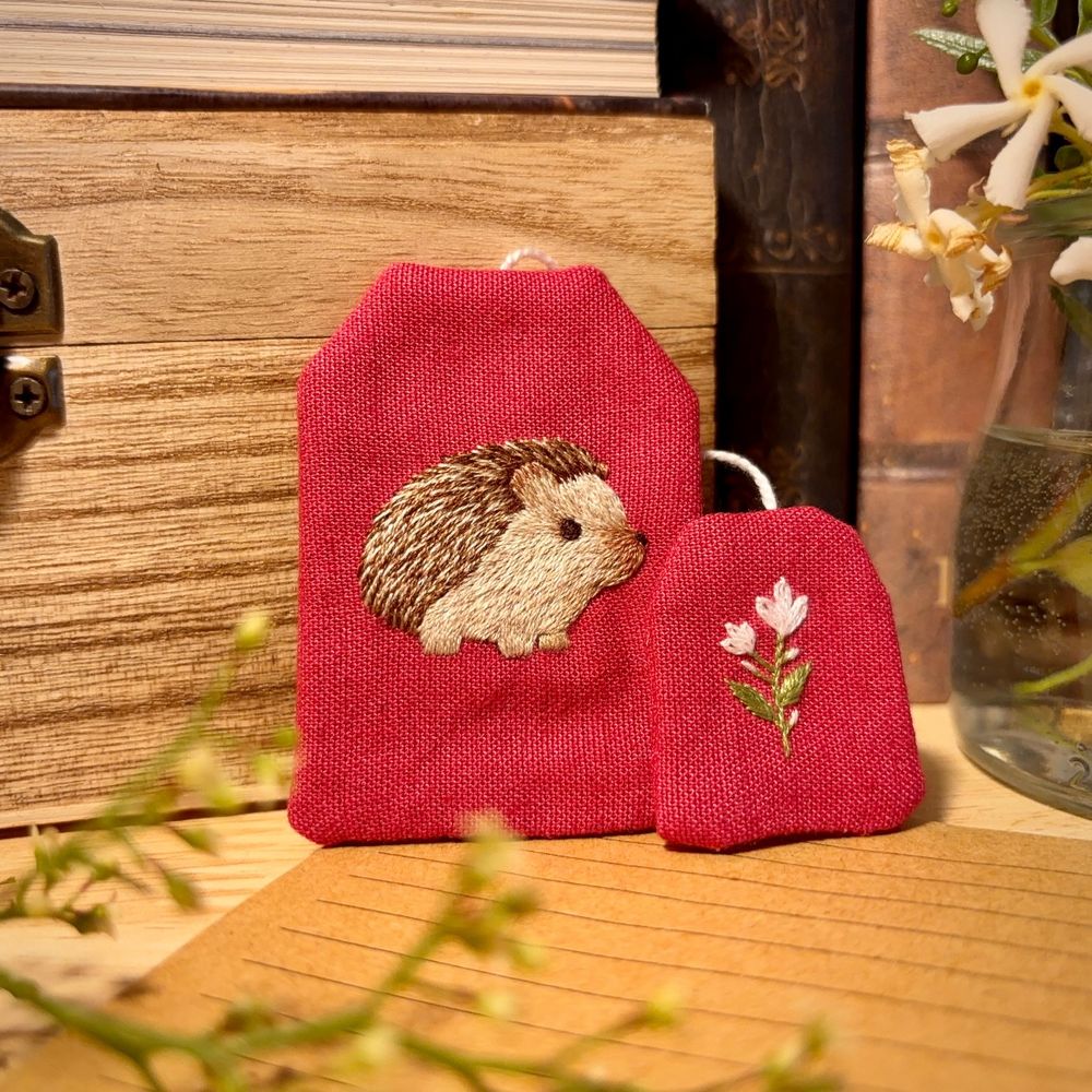 Bookmark in the shape of a tea bag, with a hedgehog embroidered on it.