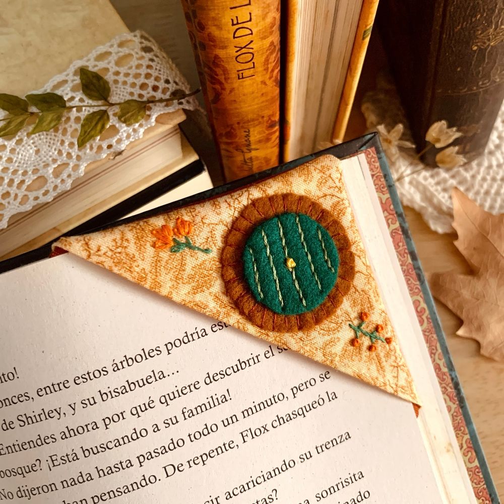 A corner bookmark made out of brownish fabric, with a green door inspired by the doors in Hobbiton. There are a couple of details embroidered with green and orange.