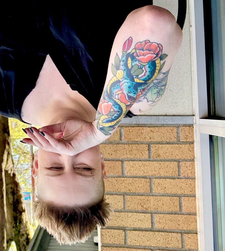 Photo of me laughing with one hand over my face, upside down so you can see the colorful tattoo on my forearm of a blue/pink/yellow eel surrounded by orange and red california poppies