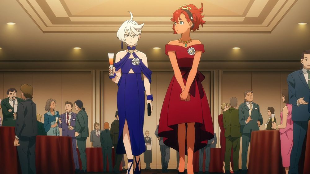 A screenshot from the series "Mobile Suit Gundam: The Witch from Mercury" (2022). It features Miorine Rembran on the left and Suletta Mercury on the right. Miorine is wearing a navy blue dress and holding an orange drink in a tall glass in her right hand, while Suletta is wearing a red dress. They are surrounded by various people wearing suits and dresses, standing at tables and talking to each other.