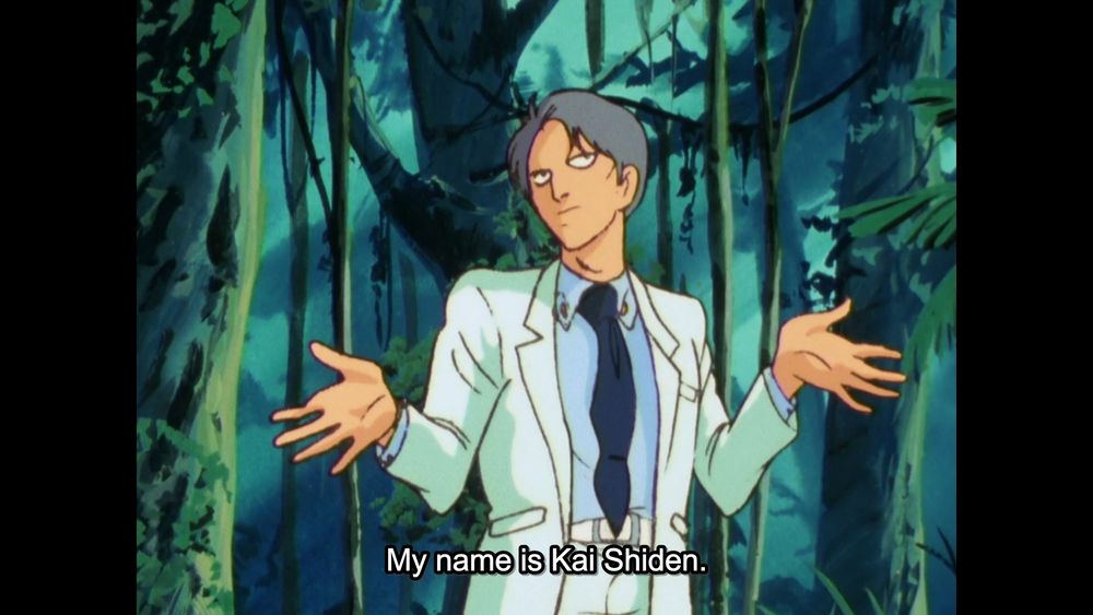 A screenshot from "Mobile Suit Zeta Gundam" (1985). It shows Kai Shiden, wearing a white suit, in the middle of a jungle, shrugging his shoulders.

The subtitles, spoken by Kai, read: "My name is Kai Shiden."