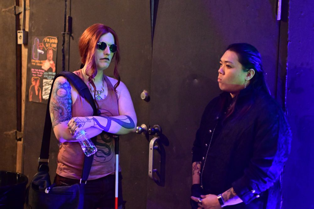 Peter in black speaking to a blind woman with red hair.