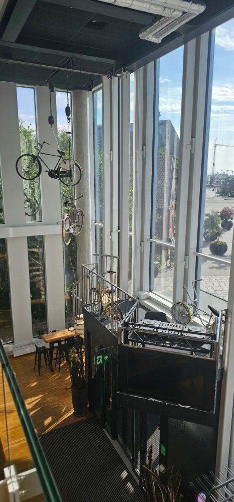 From mezzanine floor. Picture of the corner of building showing the ground floor with bicycles hanging from the roof and the sun shining in. 