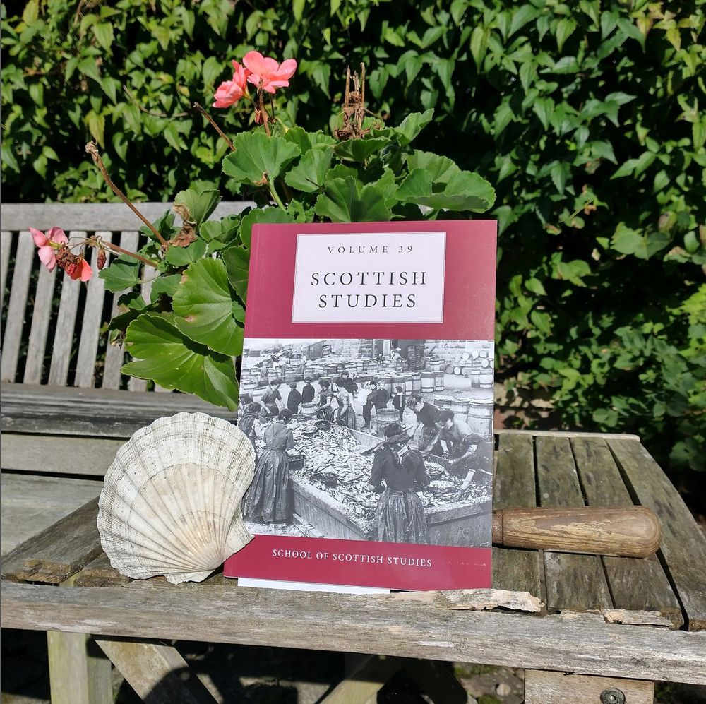 Photo. A copy of Scottish Studies volume 39 is on a wooden table. There is a seashell next to it. The cover shows a photo of herring gutters working from the Scottish Fisheries Museum. This volumes contains my first published academic article from 2022.