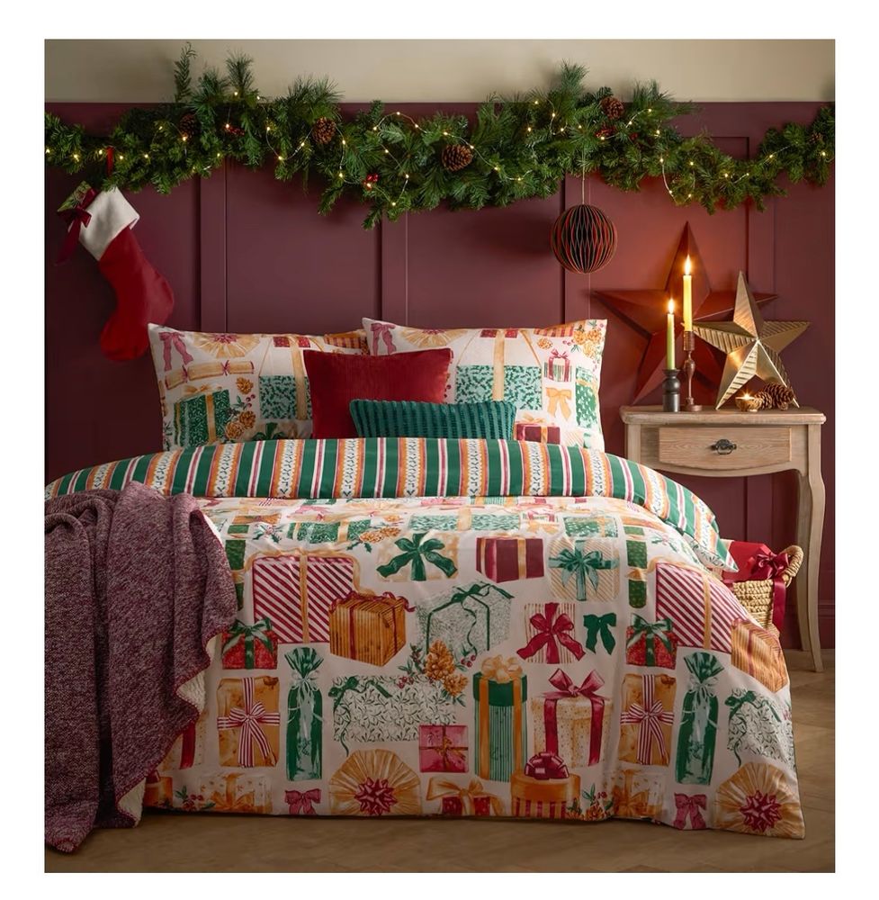 Off white bedding with presents of all shapes and sizes, mostly in green, red, and gold  