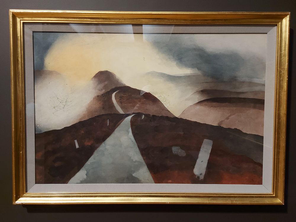 A grey road rises and falls over pinkish-brown hills before disappearing into great clouds of mist.