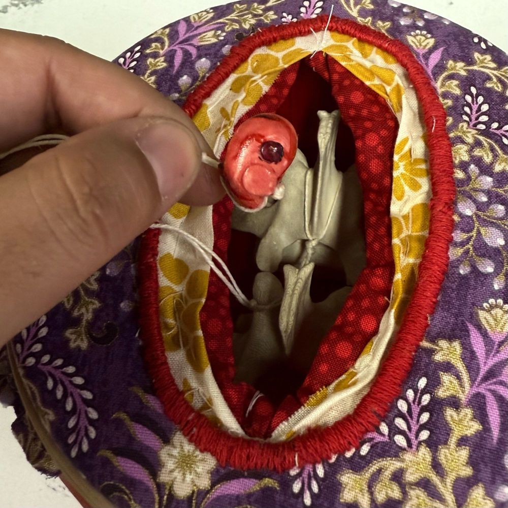 An abstract sculpture of a surgery, made of fabric and 3D printed parts. Two vertebrae peek out between layers of fabric that depict fat and body tissue. A hernia is abstracted to vaguely resemble a zygote.