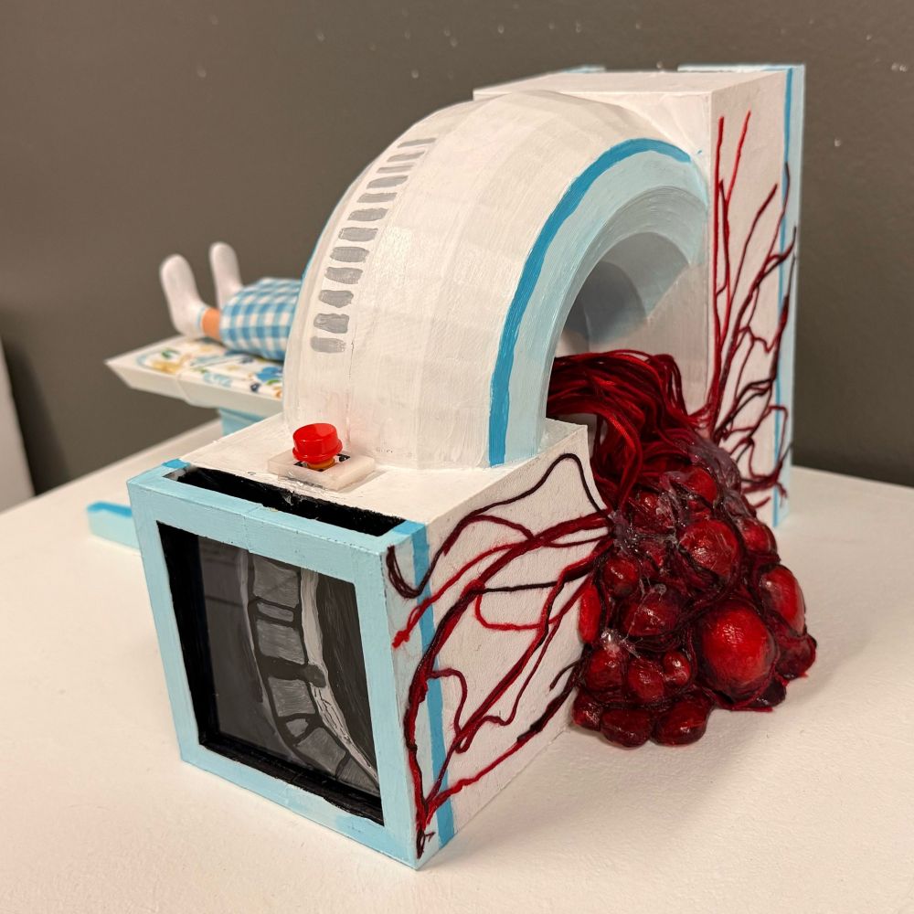 A 3D printed sculpture of an MRI machine, where abstracted gore flows out of one end, made of air dry clay and embroidery thread. A button sits atop the machine, above an MRI painted in acrylic.