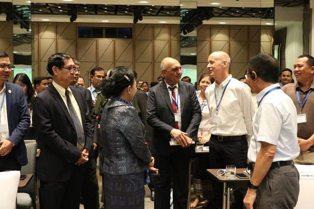 A group of attendees stand around chatting at the conference, including Dr Yok Sambath, Secretary of State of the Ministry of Health, who is being introduced the the Malaria Consortium team.