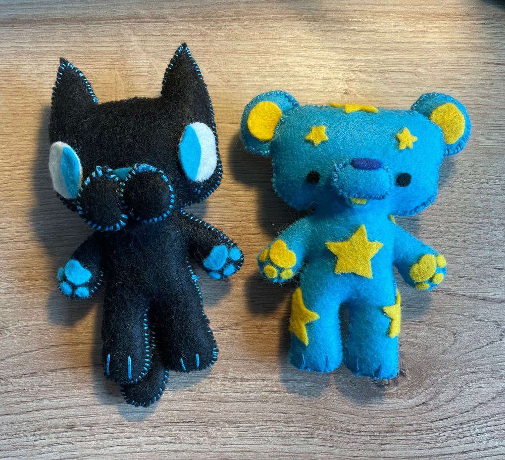Two hand sewn plushies. The right is a blue bear with yellow stars. The left is a black cat with blue eyes.
