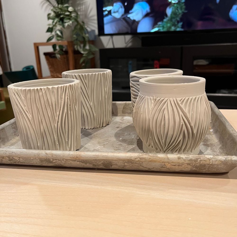 4 porcelain vessels with intricate vertical carvings. A TV is on in the background. 