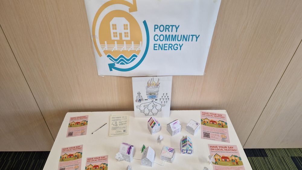 A banner on the wall saying 'Porty Community Energy'. A table with flyers and little paper houses. 