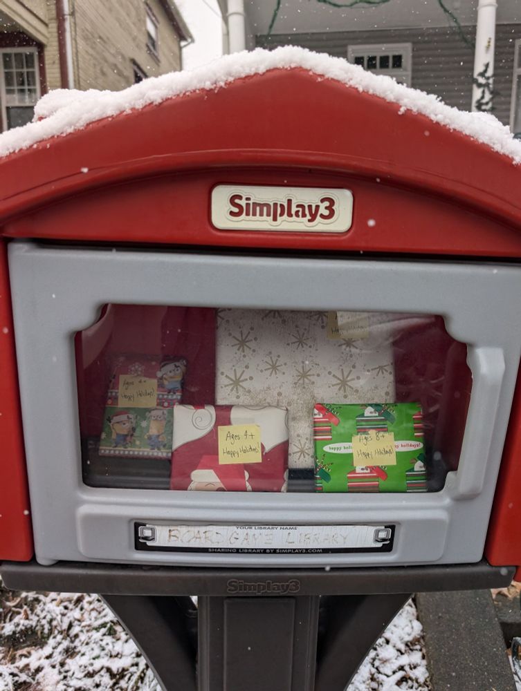 Wrapped board games in a little free library box with tags that say happy holidays and the suggested age ranges.