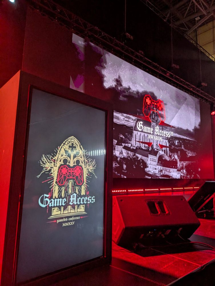The speaker desk and stage screen of the main stage of Game Access, in dark red lighting.