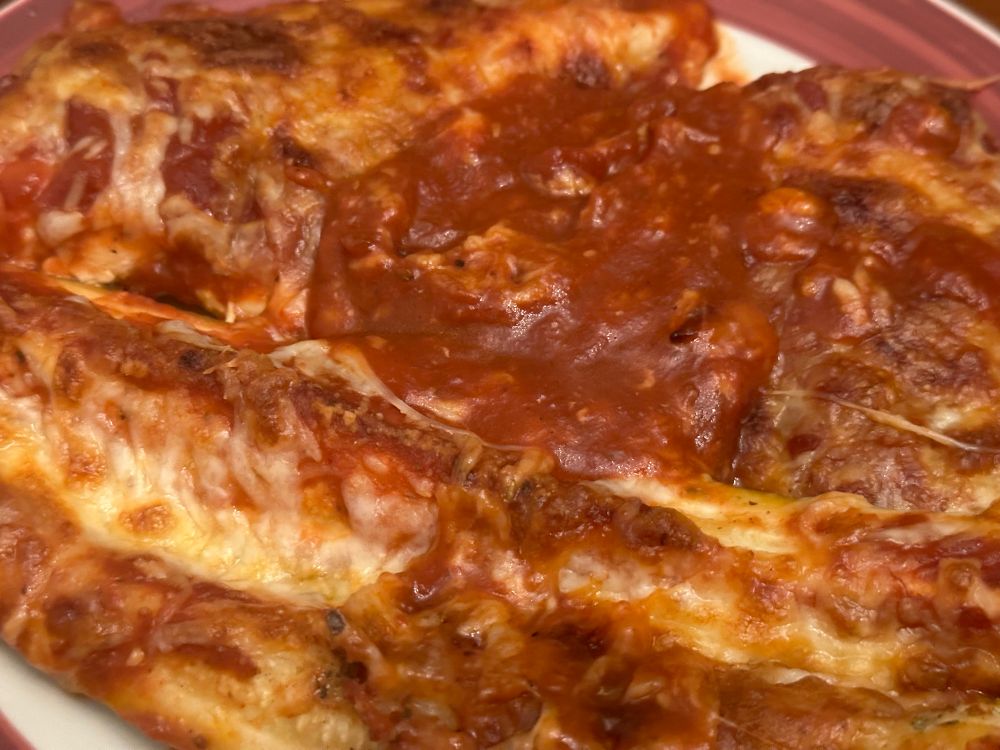 A photo of chicken parm and roasted Parmesan zucchini spears, but all you can really see is sauce and cheese 