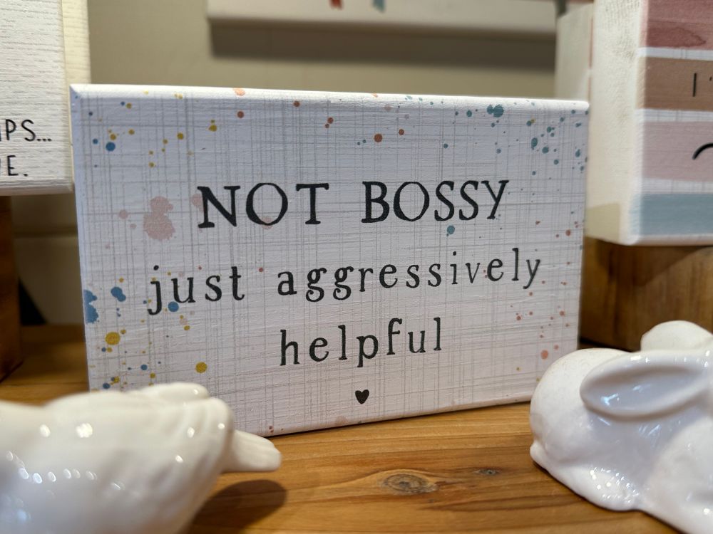 A kitschy home decor sign that says, “Not bossy, just aggressively helpful”