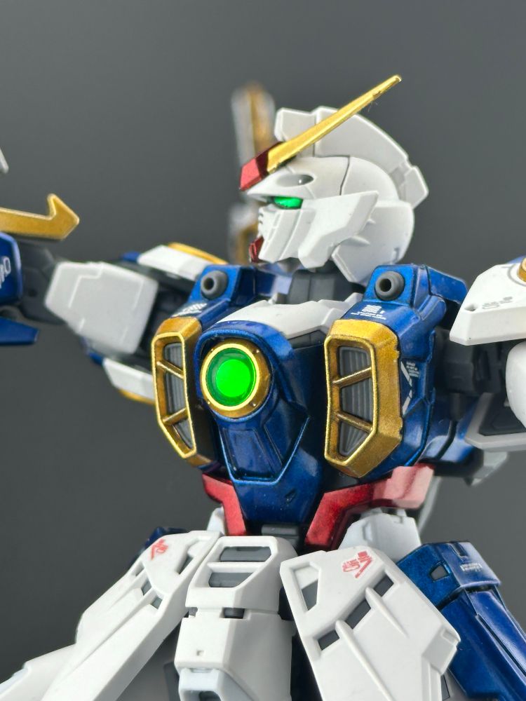 A photo of the real grade Wing Gundam plastic model kit, posed in a light box. A detail shot of the torso and head. The green circle on the chest appears to be glowing, even though it isn’t actually back lit