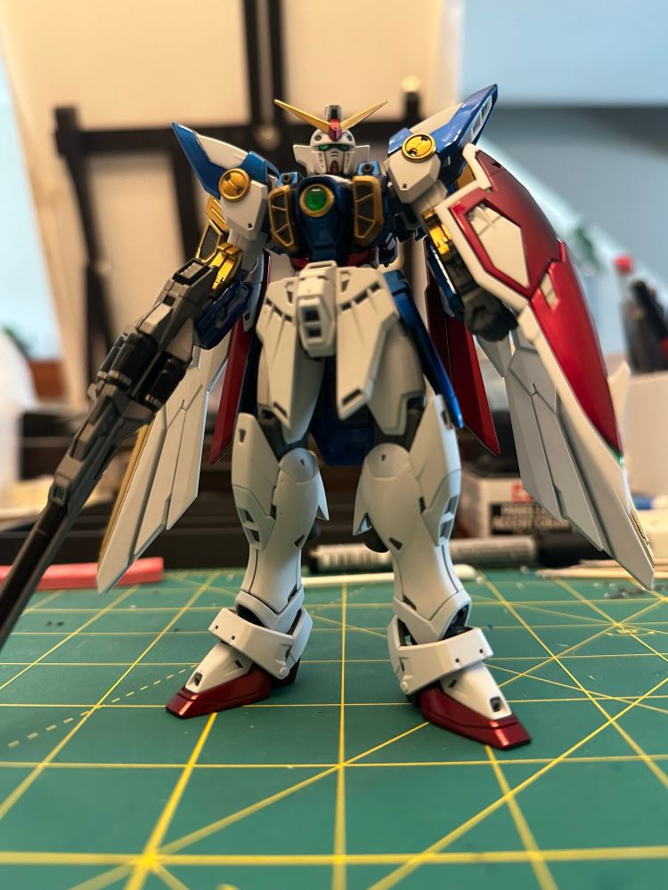 A photo of the fully built, custom painted, real grade Wing Gundam plastic model kit, standing in a neutral pose 